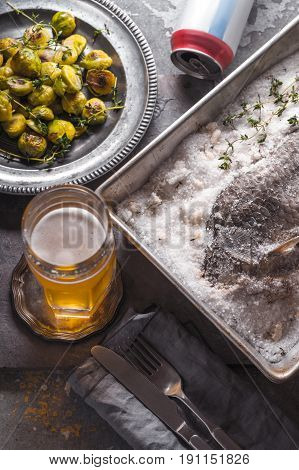 Fish baked in salt with Brussels sprouts  and beer on the stone background top view vertical