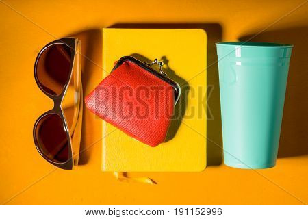 Sunglasses , purse , notebook and cup on the yellow background horizontal