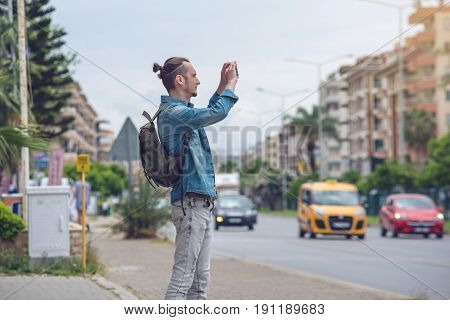 Man Traveler With Backpack Makes A Photo On Your Smartphone On A City Street