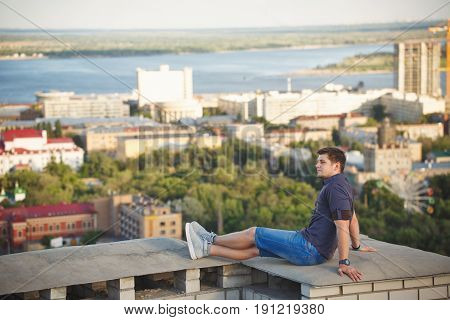 Roofer sits on the roof of a high-rise building and looks into the distance. Freedom and adrenaline.