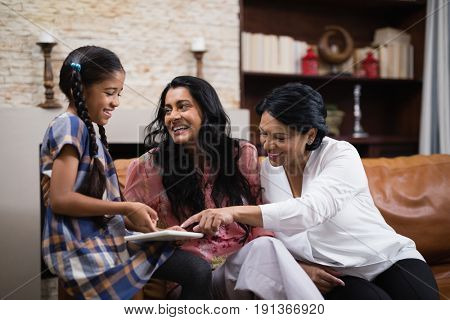 Happy multi-generation family using digital tablet while sitting together on sofa at home