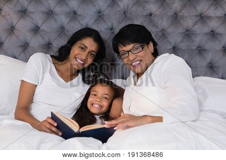 Portrait of smiling multi-generation family with book resting on bed at home