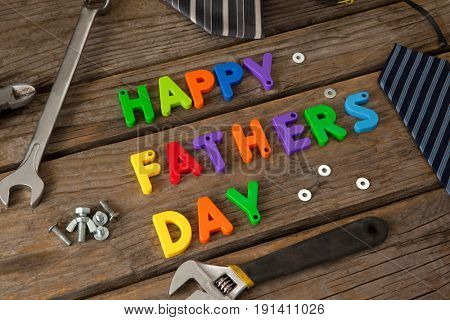 Close-up of happy fathers day blocks, tie and handtools on wooden plank