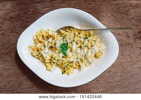 Cooked pasta campanelle sprinkled with grated cheese and greens in a white plate on a wooden table.