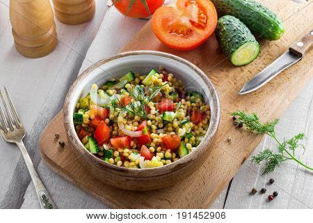 Salad made of couscous with vegetables in a bowl for healthy meal. Cooking of traditional Israeli Ptitim for lunch. Moroccan food and ingredients on a table. Top view.