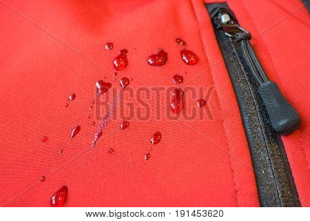 large water rain drops on red waterproof weatherproof clothes like coat or jacket. closeup macro shot of buckles zipper pocket fastener