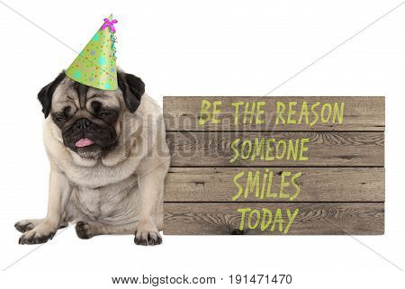 bad tempered pug puppy dog with wooden sign with text be the reason someone smiles today isolated on white background