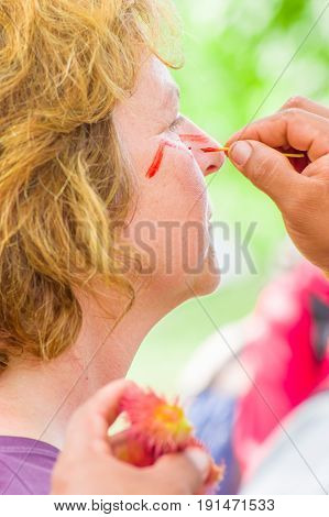 CUYABENO, ECUADOR- MAY 06, 2017: Unidentified tourist painting her face using achiote seeds from these spiny red pods with natural color, from the amazon rainforest in Cuyabeno National Park, Ecuador.