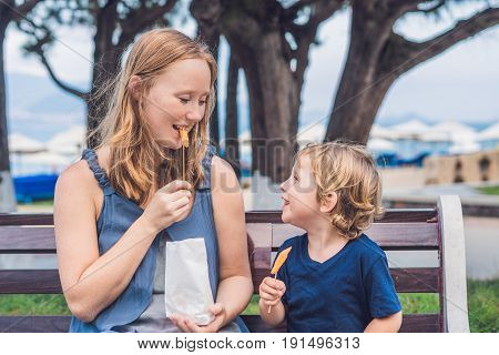 Mom And Son Eat Fried Sweet Potatoes In The Park. Junk Food Concept