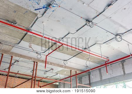 Ventilation pipes in silver insulation material and fire sprinkler on red pipe are hanging from the ceiling inside new building.