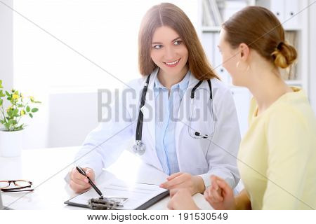 Doctor and  patient  sitting at the desk near window, sun shines