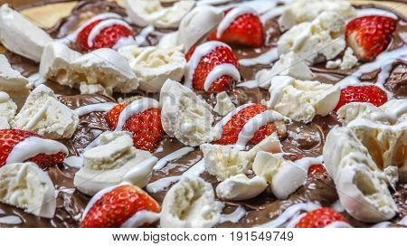 Delicious close of a brazilian pizza with cream cheese, strawberry, chocolate, meringue and milk cream over a wooden background