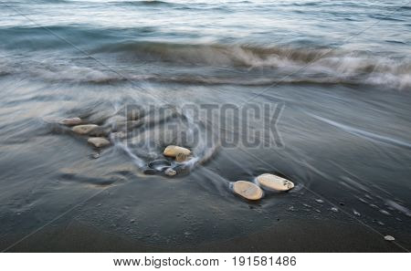 Pebbles on the beach on a black sand and flowing sea water creating nice textures. Long exposure image.