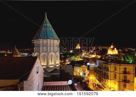 Night life in old part of Tbilisi. The Cathedral of Saint George (Surb Gevorg) 13th-century Armenian church in the historical quarter. The Holy Trinity Cathedral (Sameba) and Metekhi church with illumination on background. Georgia.