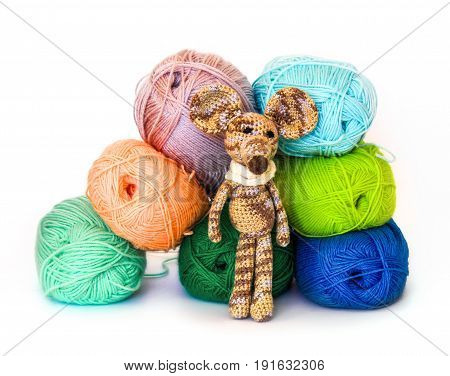 small colorful knitted toy mouse in a white scarf playing with colored yarn threads of wool Bright children's toy clew knitted mouse between skeins