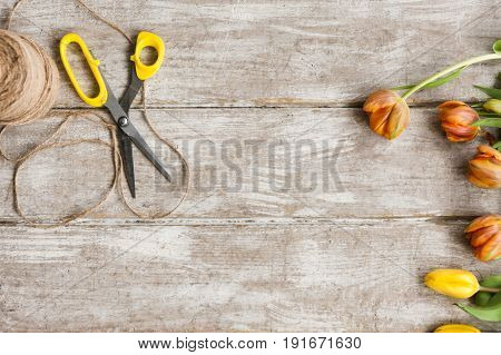 Tulips, scissors and rope on wooden background. Top view on workplace with diy tools and flowers. Decoration equipment, florist, decorator, handmade concept.