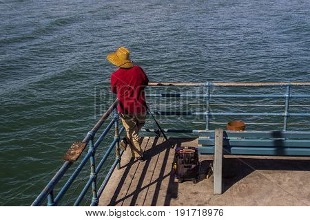 Man wearing red shirt fishing off pier with fishing rod