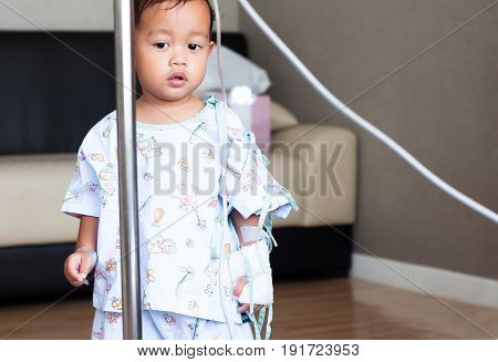 Little asia boy is stand and looking his parent in hospital room. Child with IV tube. recovering from sickness.
