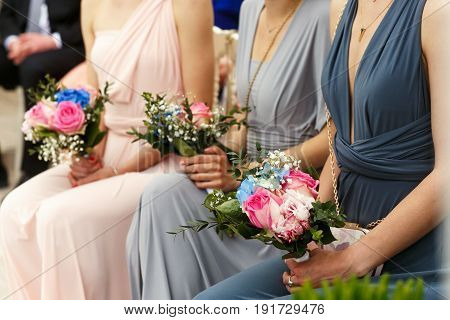 Bridesmaids In Blue, Grey And Pink Dresses Sit In The Ray