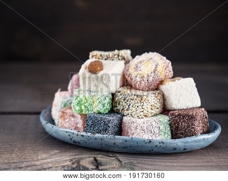 Closeup view of assortment turkish delight in blue trandy plate on dark wooden background. Copy space. Low key