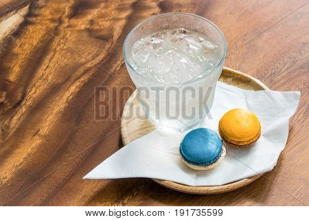 Welcome drink set with fresh ice-water blue and orange colors magaroons and white nepkin in wooden tray on wooden table.