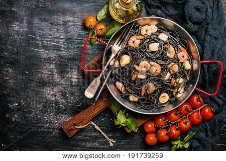 Black spaghetti with prawns and scallop in frying pan on black background, top view with copy space