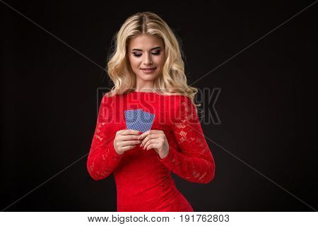 Young beautiful blond woman in a red dress with playing cards over black. Poker