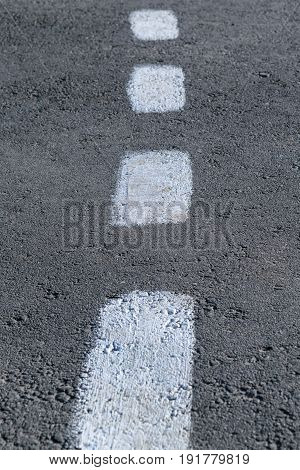On the gray asphalt paint marking. Rough intermittent white line. Dashed markings divide the road in half.