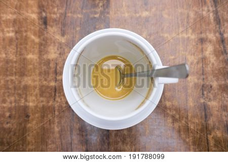 View on a white Cup of Coffee with Spoon on a brown wooden Table. 
Close-up of a creamy Coffee with refreshing effect.
Fresh Cup of Coffee. Coffee Break.