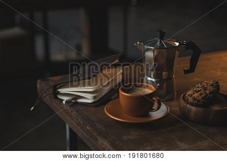 Close-up View Of Notebook With Pencil, Cup Of Coffee, Moka Pot And Chocolate Chip Cookies On Wooden