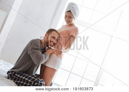 I definitely hear our baby moving. Young couple celebrating positive pregnancy test results while standing in bedroom in the morning.
