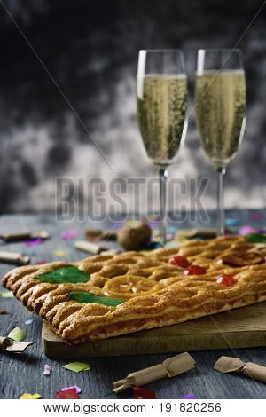 closeup of a coca de Sant Joan, a typical sweet flat cake from Catalonia, Spain, eaten on Saint Johns Eve, on a rustic table, a pair of glasses with champagne, firecrackers and confetti