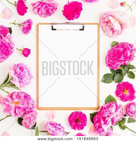 Floral frame of pink flowers and clipboard with paper on white background. Flat lay, top view. Floral pattern of pink flowers