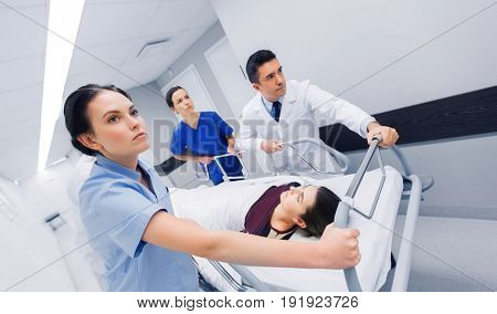 profession, people, health care, reanimation and medicine concept - group of medics or doctors carrying woman patient on hospital gurney to emergency