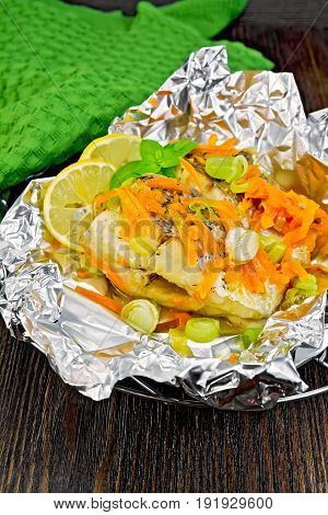 Pike with carrots, leek, basil and slices of lemon in foil on the lattice, a green towel on a dark wooden board