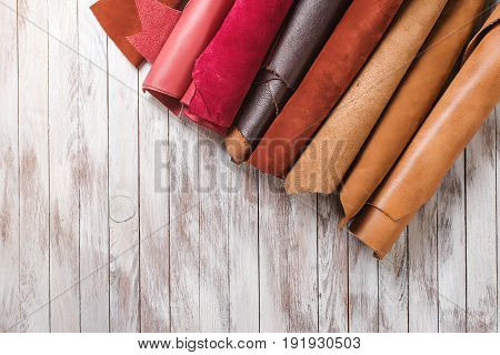 Multicolored leather in rolls on the wooden background.