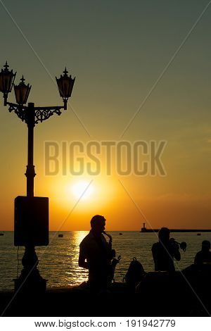 The musician playing the saxophone on the coast a beautiful sunset.