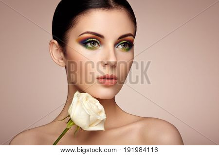 Portrait of beautiful young woman with rainbow make-up. Girl summer. Long eyelashes vivid colorful eyeshadows. White rose. Multicolored