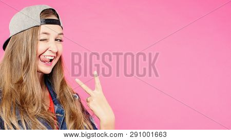 Studio Portrait Of Smiling Hippster Brunette In Cap Holding Fingers.