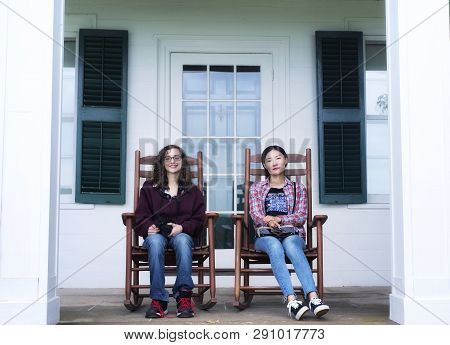 A Caucasian And Chinese Woman Sitting On Wooden Rocking Chairs On The Porch Of The Historic Hillstea