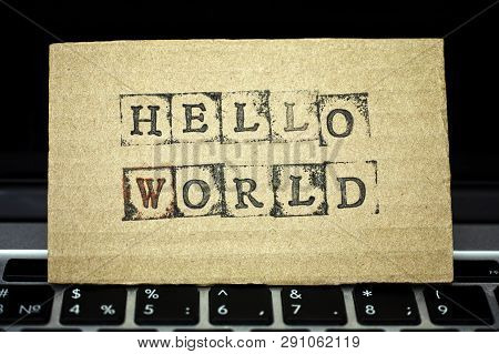 Сardboard With Words Hello World Maked By Black Alphabet Stamps Standing On Laptop Keyboard.