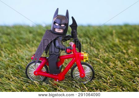 Paphos, Cyprus - October 26, 2016 Lego Batman Minifigure With Batarang Riding Red Bike On Grass Back