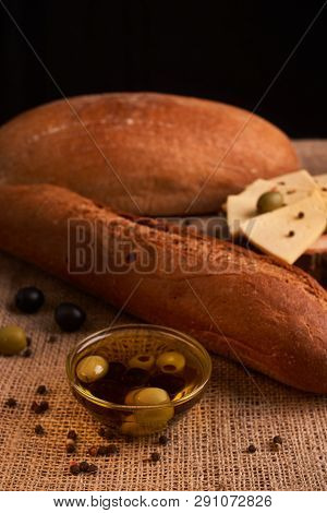 Fresh Bread Baguette With Olive Oil, Olives. Cheese And Rosemary On Wooden Background. Teasty Breakf