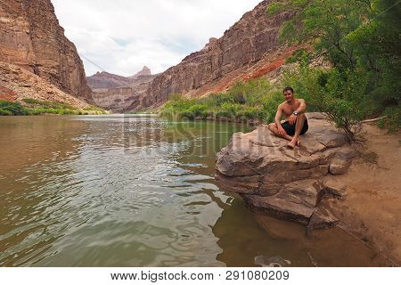 Young Man Resting By The Colorado River Just Above Hance Rapids During A Multi-day Hike In Grand Can