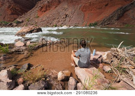Young Woman Resting By The Colorado River At Hance Rapids During A Multi-day Hike In Grand Canyon Na