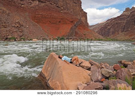 Young Woman Resting By The Colorado River At Hance Rapids During A Multi-day Hike In Grand Canyon Na