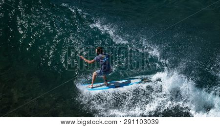 MAUI / USA - 14 DECEMBER 2018: Young longboard surfer tries to do nose riding trick while glides on the wave at Honolua surf spot on the north of Maui, Hawaii