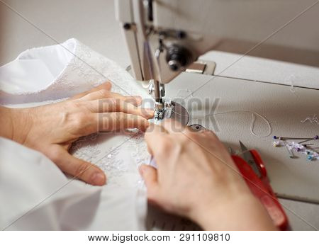 Female Hands Stitching White Dress At Workplace With Pins, Threads And Scissors On Background. Seams
