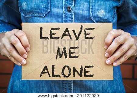 Woman Hands Holding Piece Of Cardboard With Words Leave Me Alone Against Brick Wall Background.