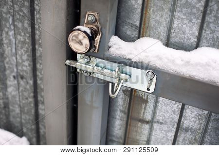 Metal Door With Door Knob And Bolt Covered Snow. Close-up.